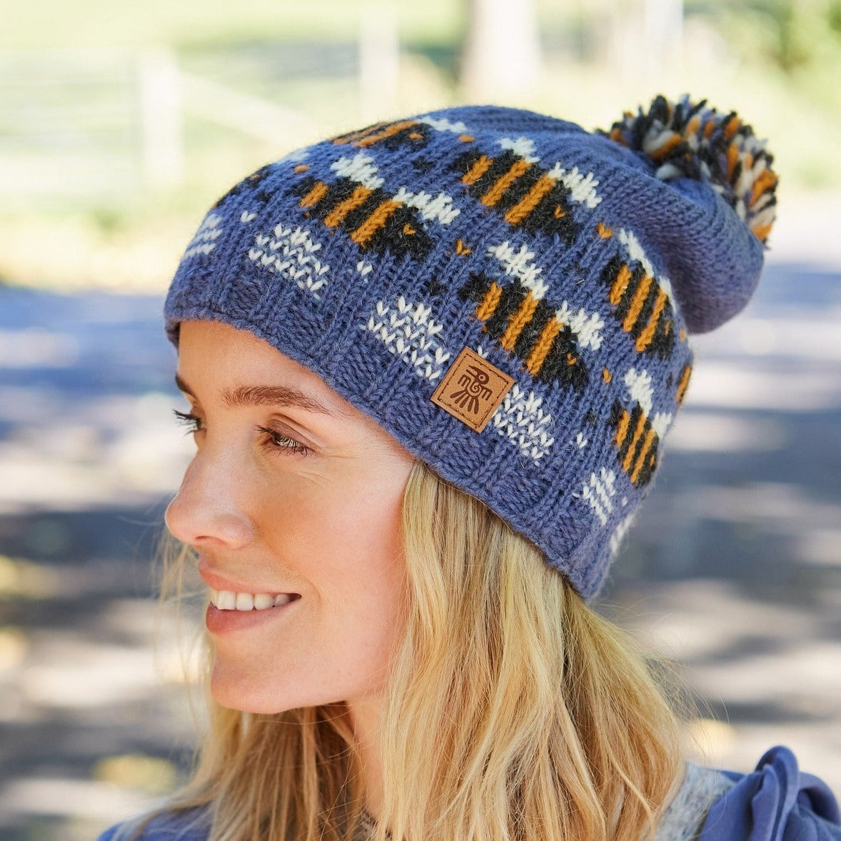 A person wearing a blue and multicolored striped beanie hat with a beehive pattern and a pom-pom on the top.