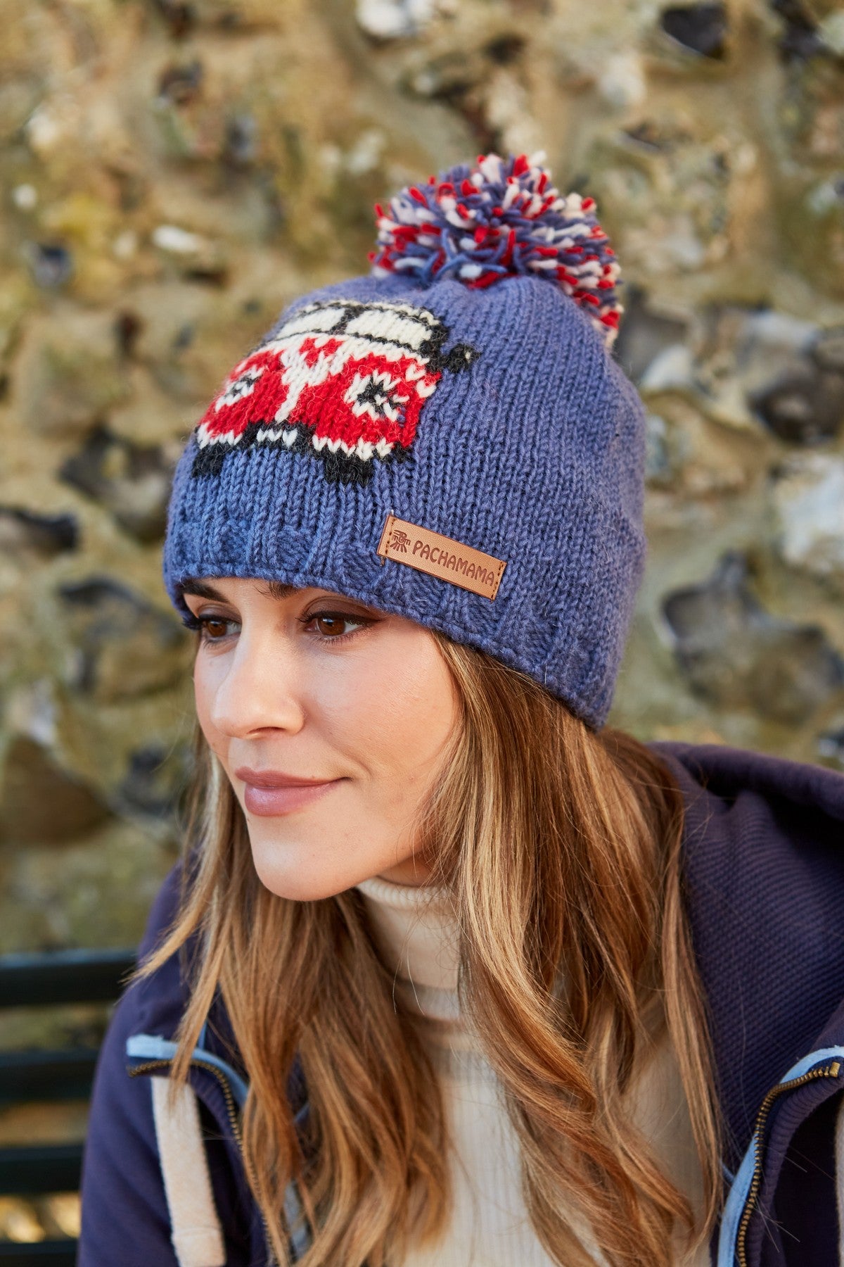 A woman wearing a gray bobble beanie with a camper van pattern and a brown leather patch on the brim.