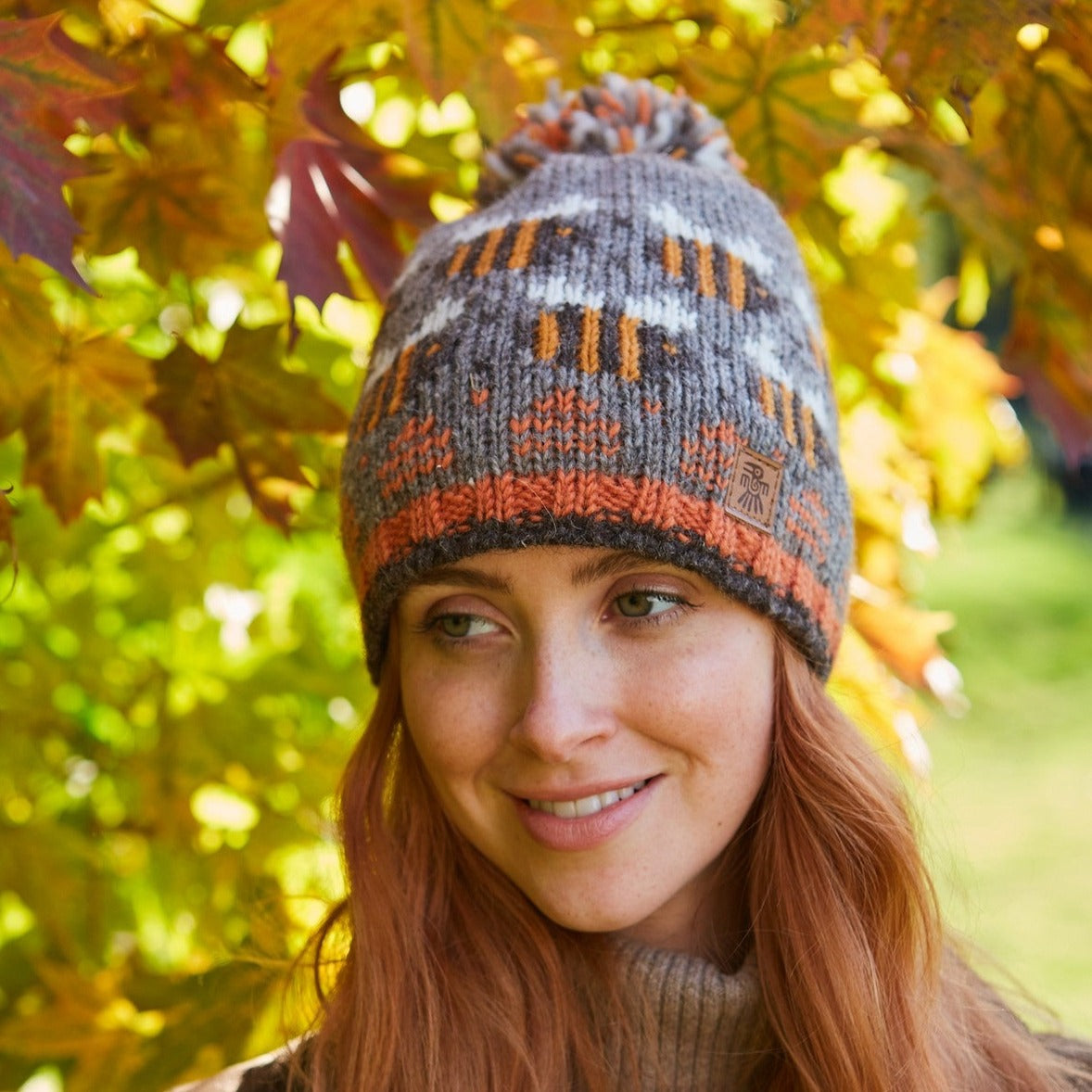 A person wearing a brown and multicolored striped beanie hat with a beehive pattern and a pom-pom on the top.