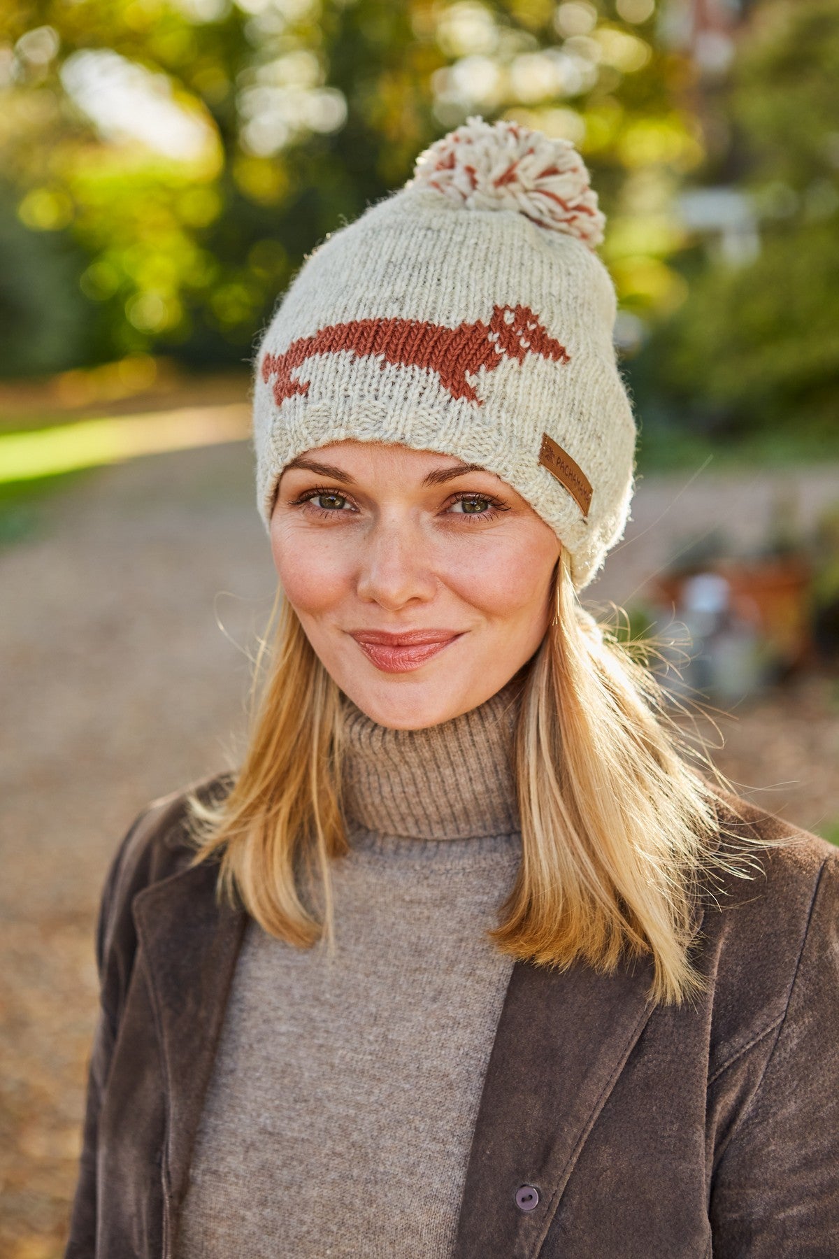 A woman wearing a beige bobble beanie with a brown sausage dog pattern.