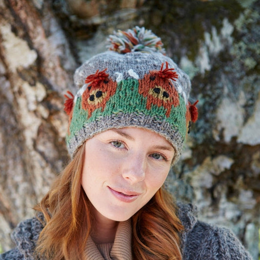 A person wearing a multicolored wool bobble hat with a Highland cow design.