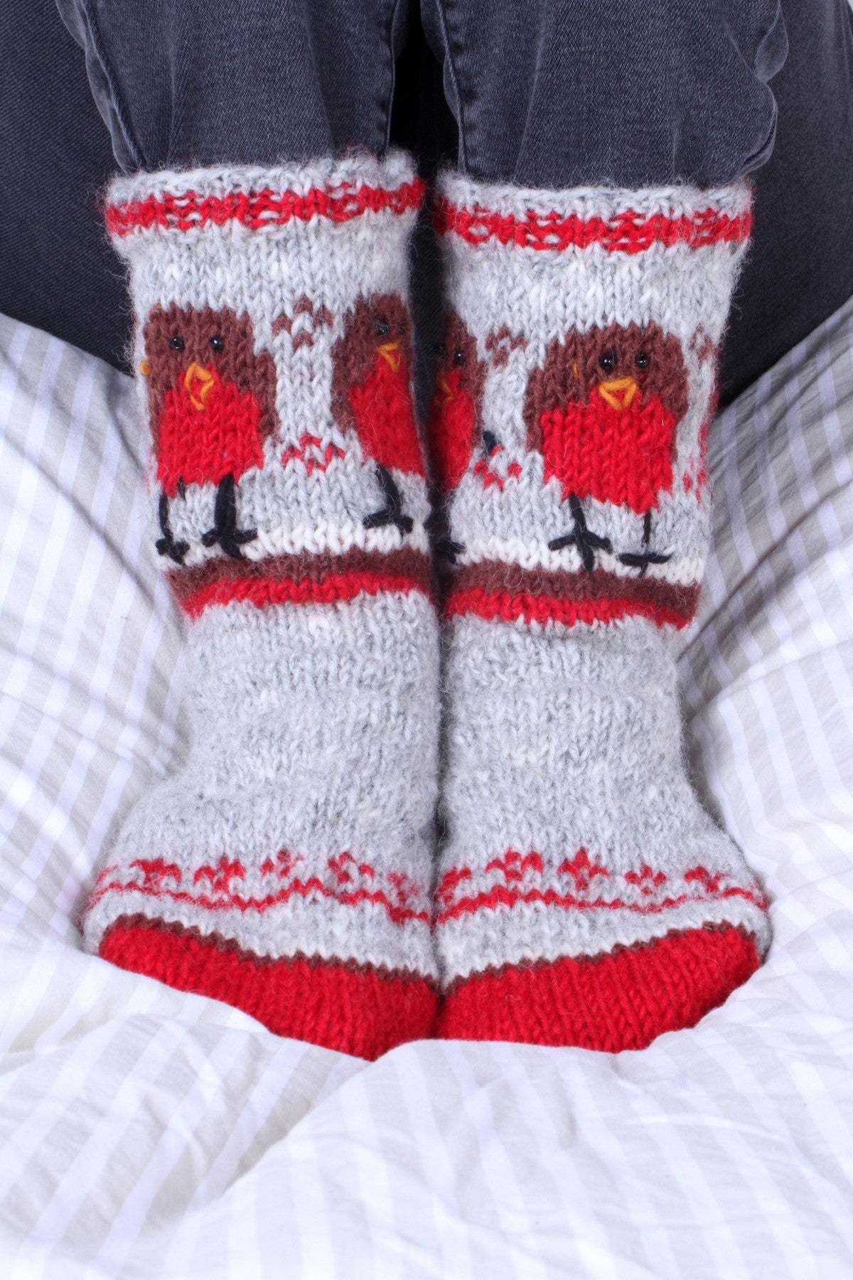 Pair of Pachamama Wool Sofa Socks worn over black jeans whilst sitting on a bed