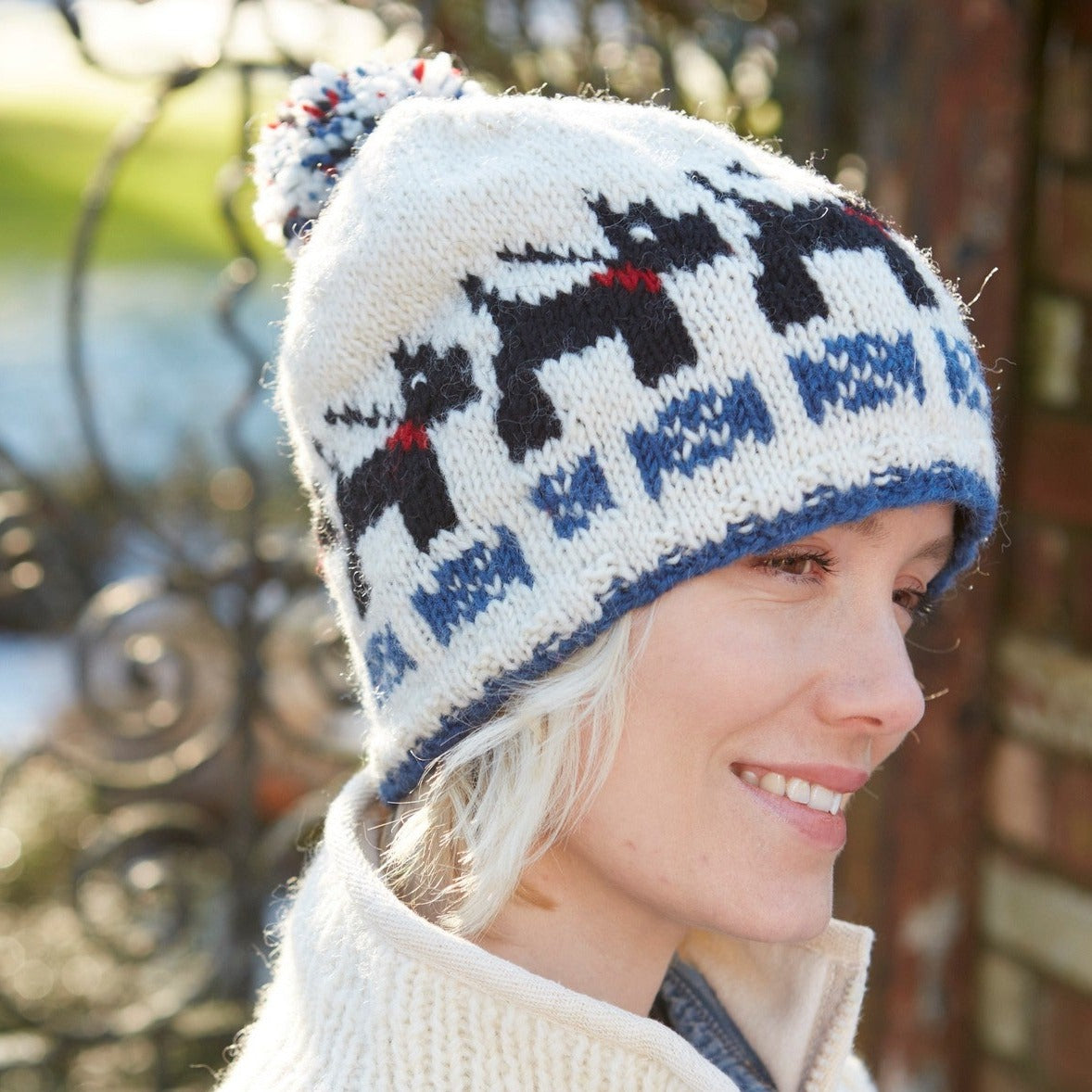 Lady wearing a white bobble beanie with black Radley type dogs.
