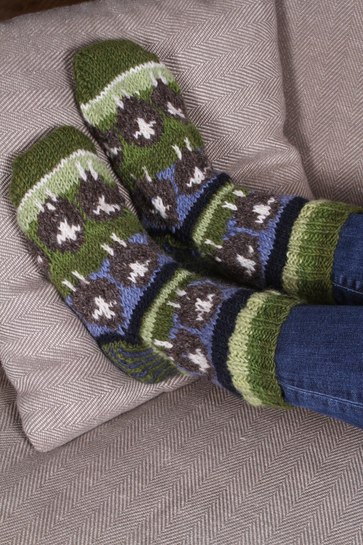 Pair of Pachamama Herdwick Flock of Sheep Sofa Socks being worn over jeans whilst relaxing on a sofa