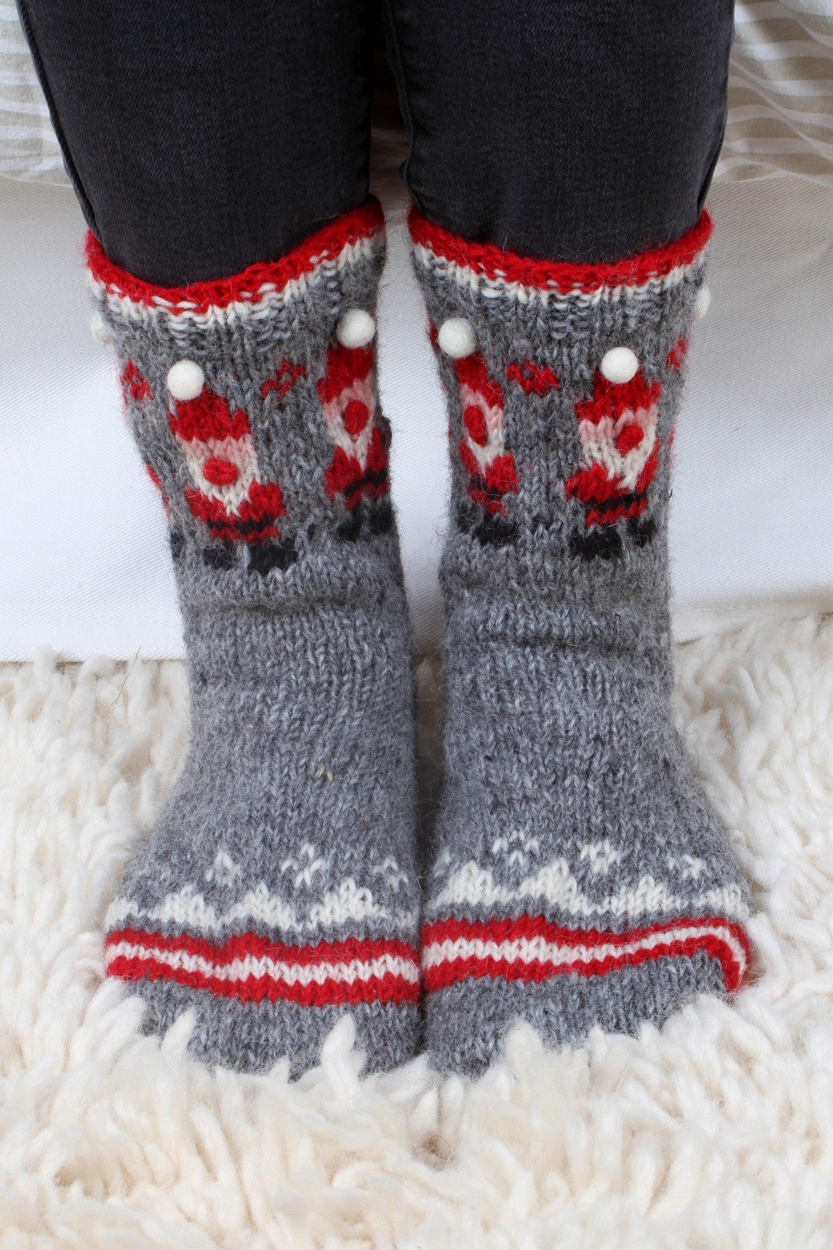 Pair of Pachamama Santa Sofa Socks being worn over a pair of black jeans whilst standing on a wool rug